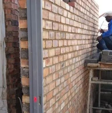 Face-brick wall under construction with a white door frame and a builder working from a scaffold