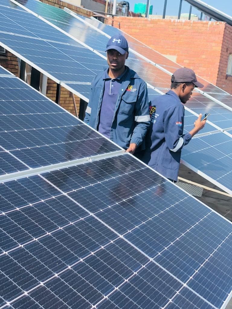 Two ZEPS technicians in navy jackets on a rooftop solar array