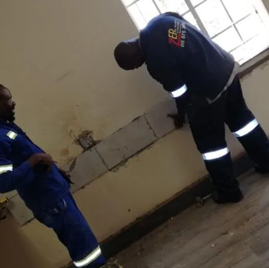 Two technicians in navy overalls inspecting an interior wall during a renovation