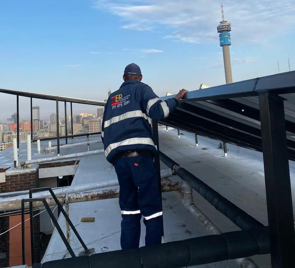 Technician in a ZEPS navy jacket on a rooftop, with the Hillbrow Tower on the skyline