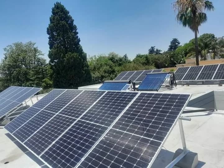 Rooftop solar photovoltaic panels with two solar geyser collectors and trees behind the roof