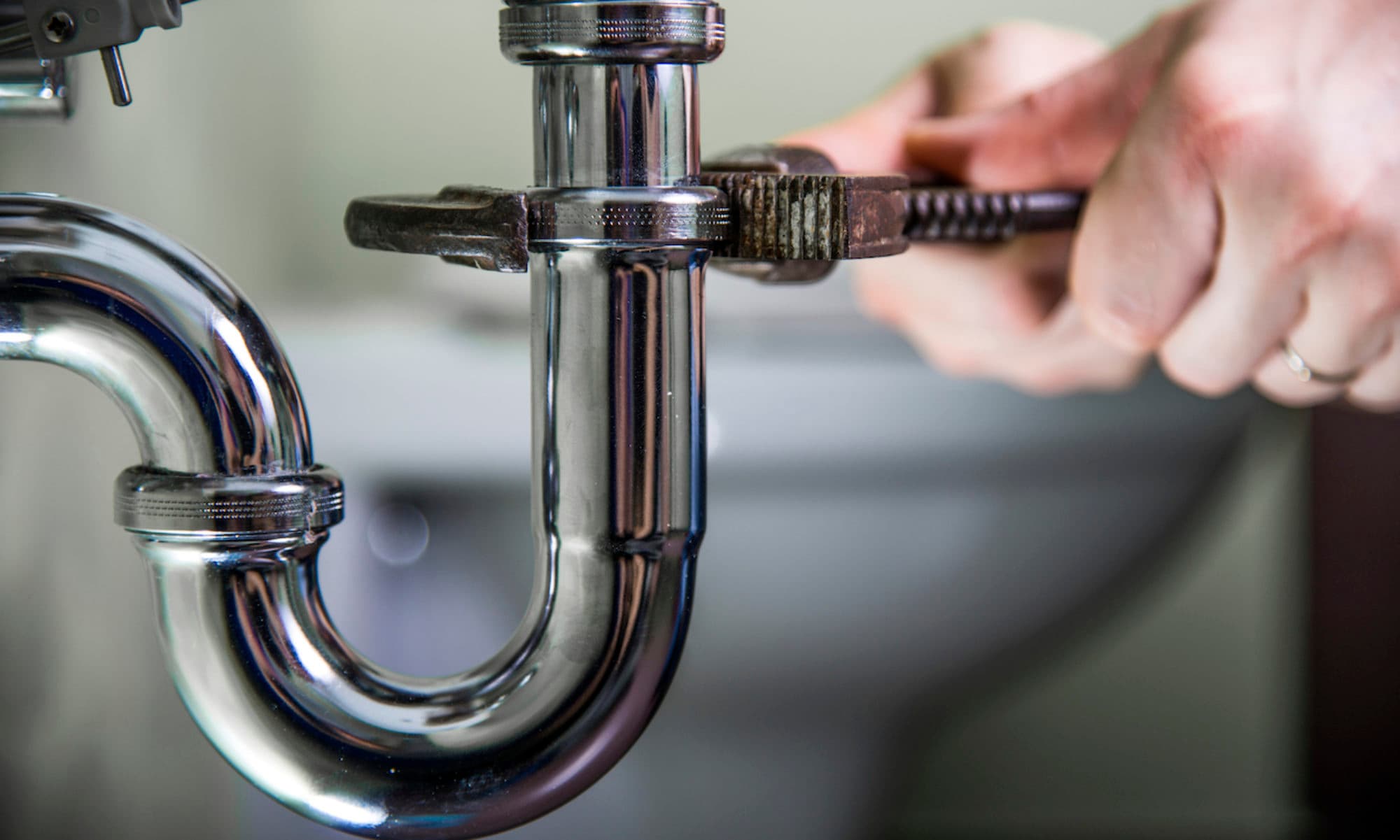 Plumber tightening a chrome trap with a pipe wrench